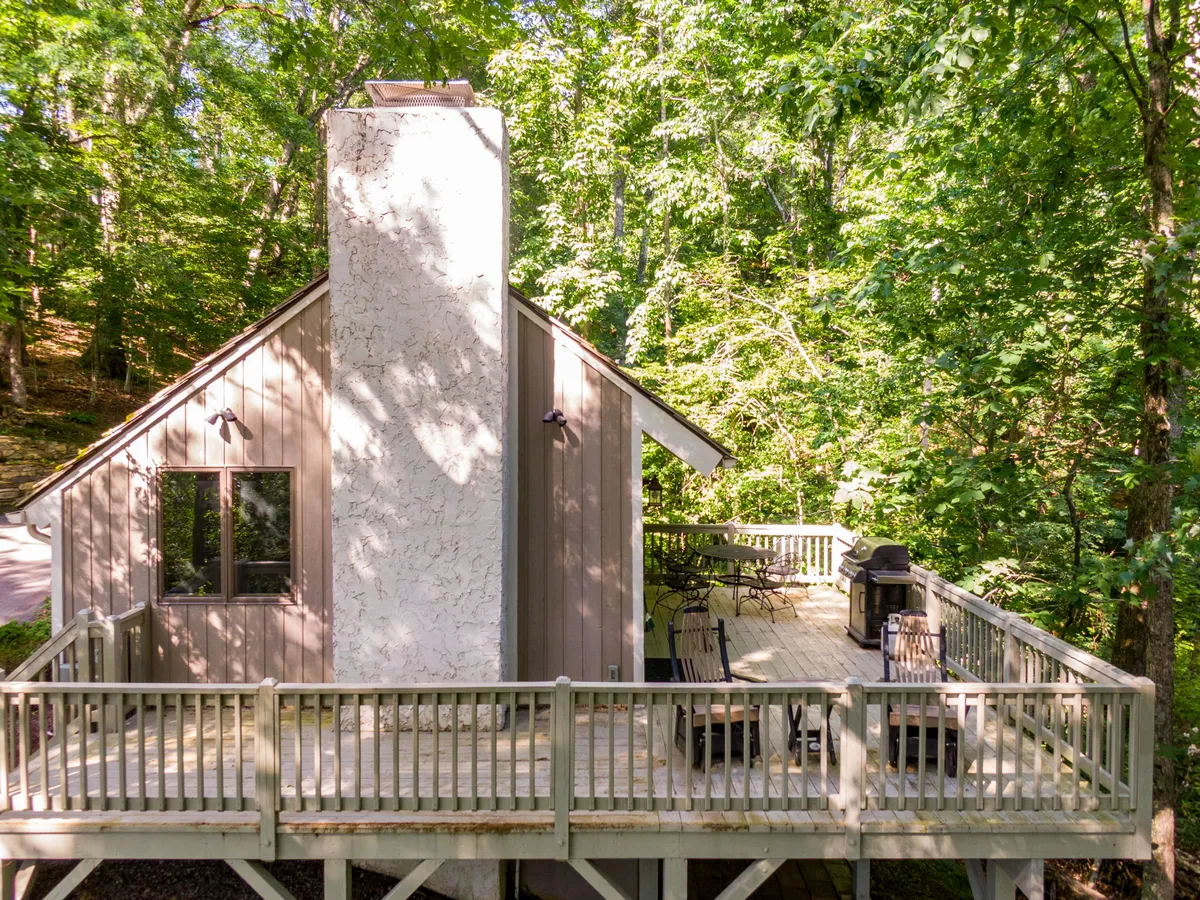 The hero image showcases the exterior of a charming mountain cottage surrounded by lush greenery, with a spacious wooden deck, a rustic chimney, and inviting outdoor seating. The deck is oriented to capture sunset views, and the tranquil setting highlights opportunities for dining outdoors and relaxing in nature.