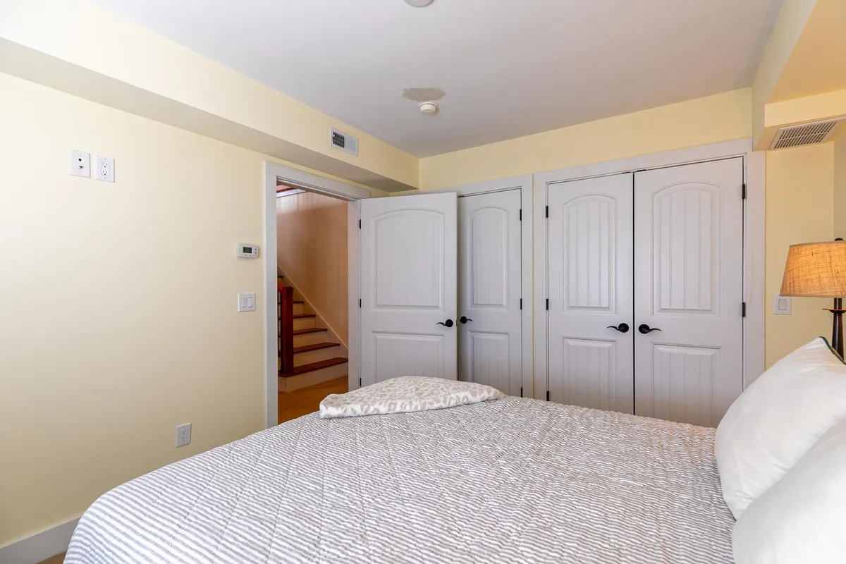 A tranquil bedroom featuring a comfortable Queen bed, two doors (suggesting access to other parts of the lower level or storage), and a nearby staircase. The space is warmly lit and arranged for relaxation and restful moments, with hints of forested views visible through the windows.