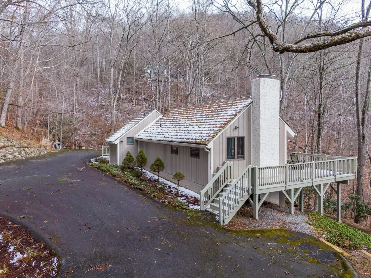 An inviting view of the house exterior, with a spacious deck nestled among tall trees. The setting feels peaceful and private, suggesting opportunities for outdoor relaxation, sunrise viewing, and direct access to surrounding trails.