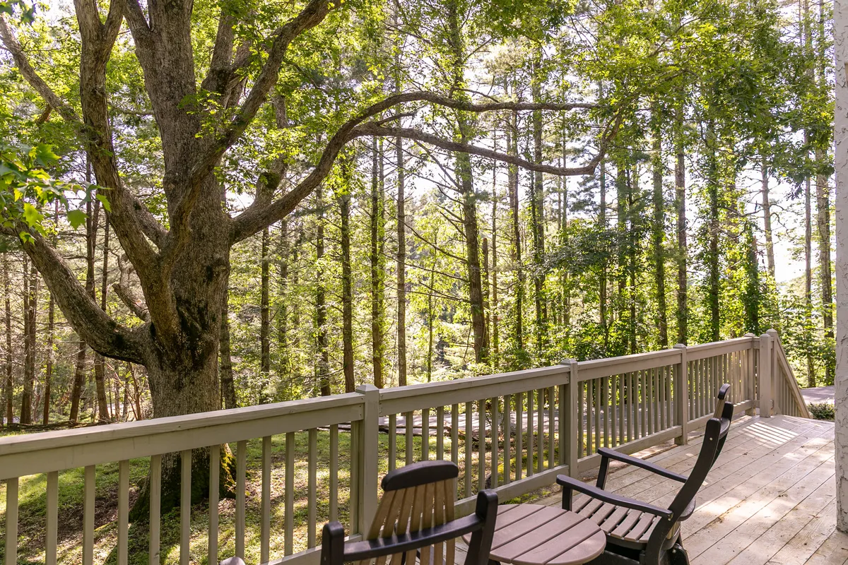 A tranquil view of the deck, showing chairs overlooking the surrounding trees and forest. The large deck railing and dappled sunlight through the canopy create an inviting atmosphere for relaxation and socializing.