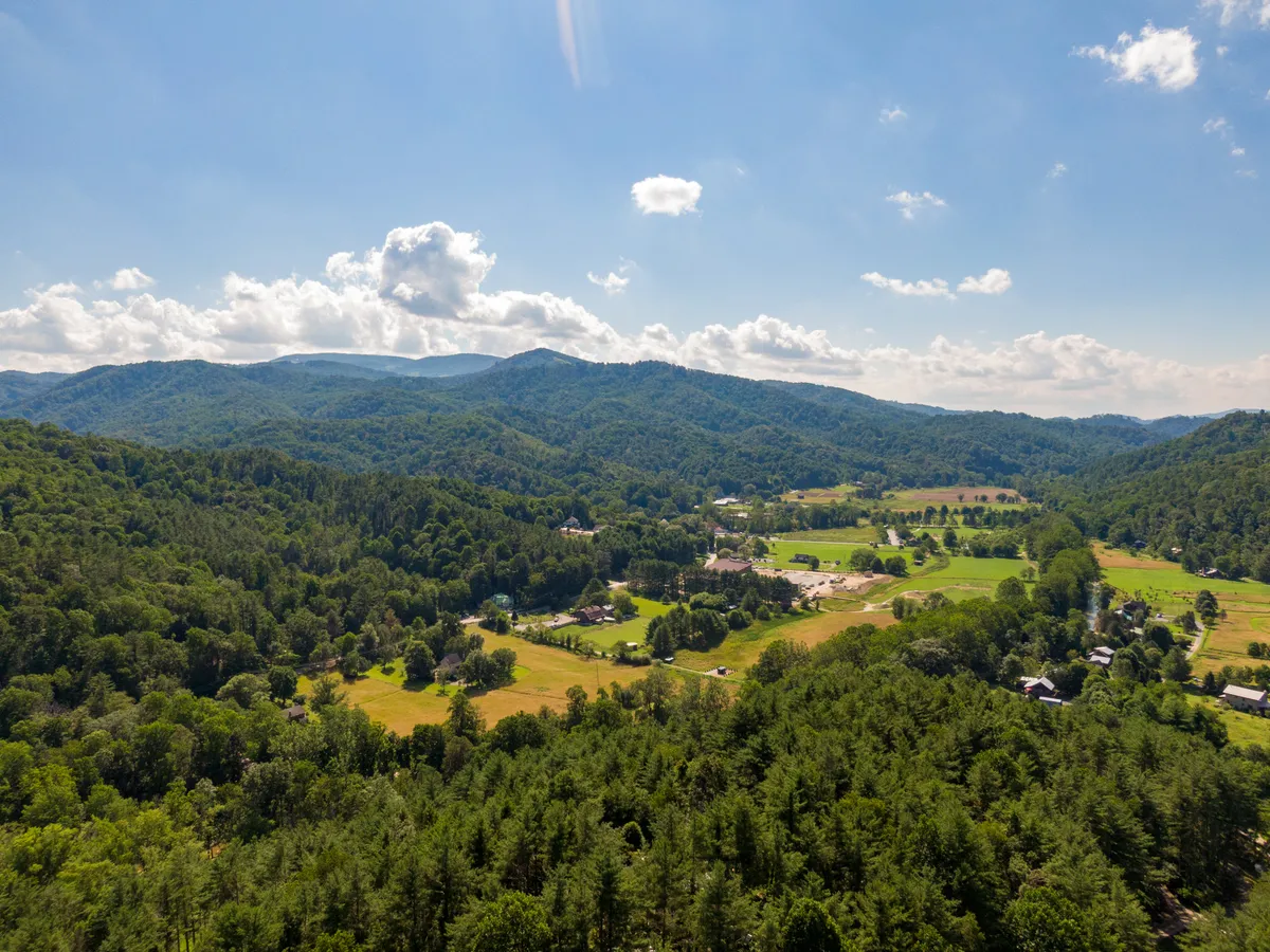 A sweeping view of a mountain range with lush green valleys, a small village nestled in the landscape, and farmland in the foreground. The early morning atmosphere is calm and inviting, suggesting easy access to local communities and scenic beauty.