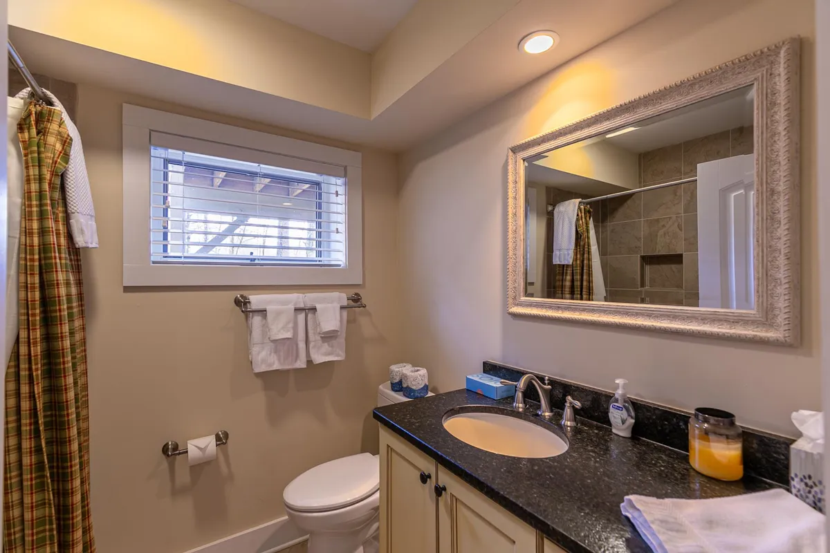 A well-lit full bathroom with a sink and countertop, mirror, window allowing in natural light, fresh towels, and a shower with a curtain. The space feels fresh and welcoming, perfect for a relaxing bath or refreshing morning routine.