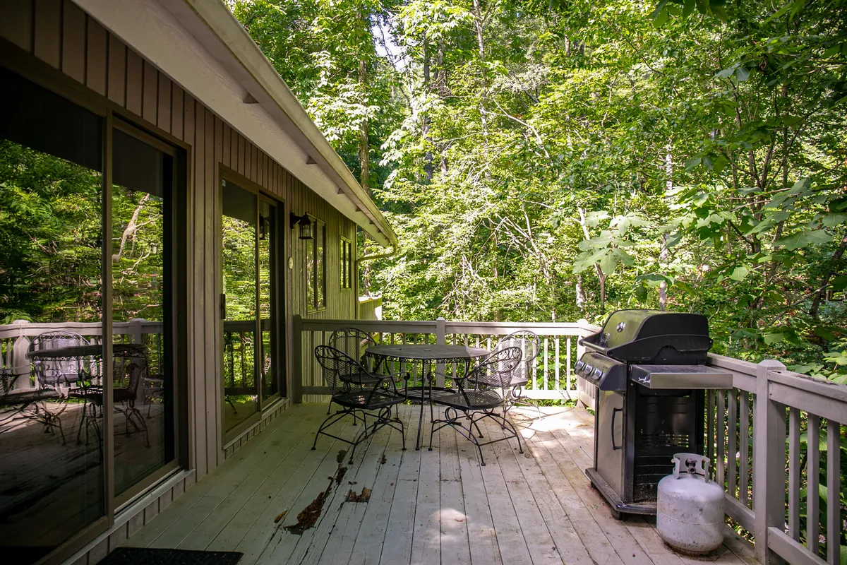An exterior shot focused on the outdoor dining set and grill nestled among lush greenery. The table is set for al fresco meals, and the gas grill is clearly visible, emphasizing the social and culinary possibilities of the deck space.