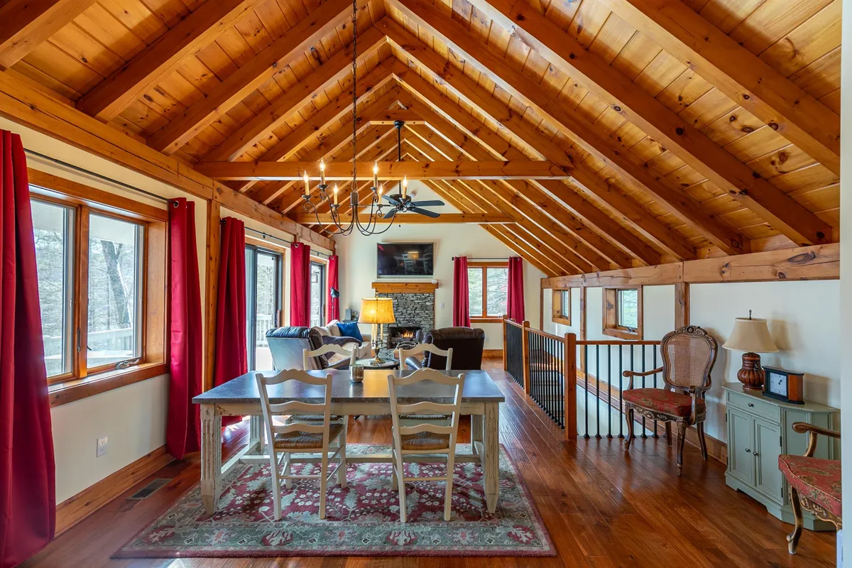 An interior view highlighting a dining table under a chandelier, a crackling fireplace, and large windows letting in natural light. The space is arranged for family meals, entertaining, and cozy gatherings.